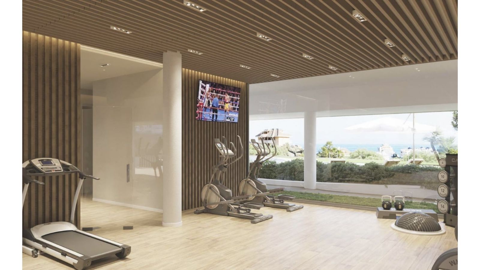 Gimnasio moderno con cinta de correr, elípticas y vistas al mar.